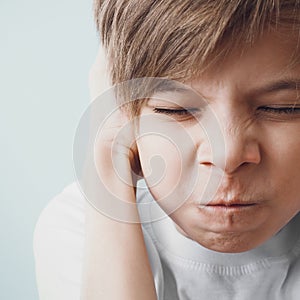 Boy closes his ears with his hands and frowns with his eyes closed