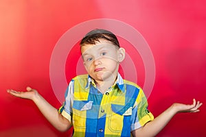 A boy in a color shirt shrugs and spreads his arms to the side, on a red background