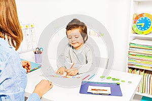 Boy colors shapes during ABA with therapist near photo