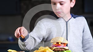Boy comes to table on which is fried French fries and begins to eat fast food.