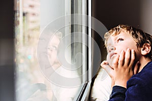 Boy confined at home by the coronavirus crisis in Spain, looks bored out the window without being able to leave home