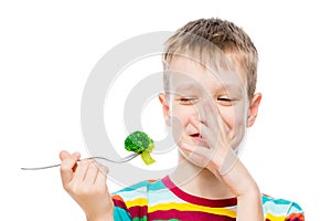 The boy with contempt looks at broccoli, portrait is isolated on white