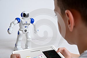 Boy controls robot using tablet on desk. Illustrating education, technology, innovation