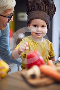 Boy in cook hat spending happy time in the kitchen with his grandmother