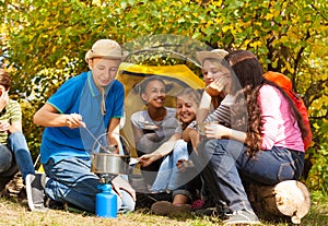 Boy cooking soup in pot for friends at campsite