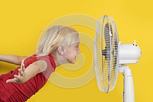 Boy cools off with ventilator. Portrait on yellow background. Summer heat