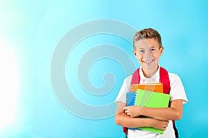 Boy with copybooks and backpack against color background