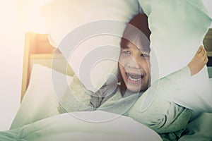 Boy covering ear with pillow after waking up from nightmare sleepless insomnia night on bed in the morning