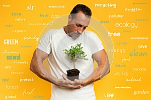 Boy cradles a small tree ready to be planted. yellow color background. concept of forestation, ecology and conservation