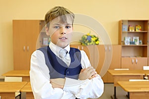 Boy with crossed arms stands in empty classroom photo