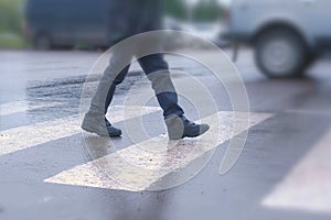 Boy crosses the road at a pedestrian crossing in the rain. Legs close-up.