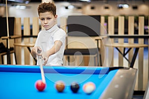 Boy with cue stick stands near pool table aiming photo