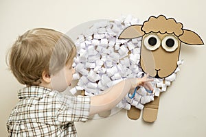 The boy cuts a paper sheep. Early education, fine motor skills.