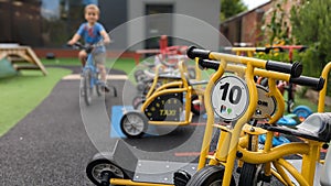 A boy cycles his bike past a row of bikes & trikes on a school playground photo