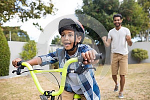 Boy cycling with father standing in background