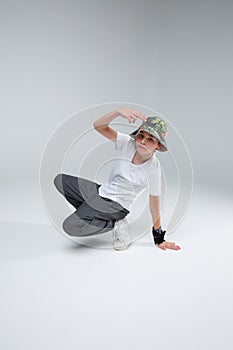 A boy, dancing in the style of breakdance, sitting in a squatting position, and holding hand near head.