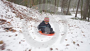 A boy in dark overalls is spinning on a sled down in the woods