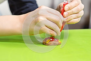 Boy decorates a cinnamon cookie. He holds a tube of red icing in his hands and squeezes it on the cake.
