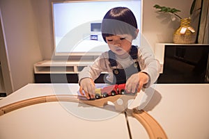 A boy in denim overalls is playing with a wooden train toy attentively