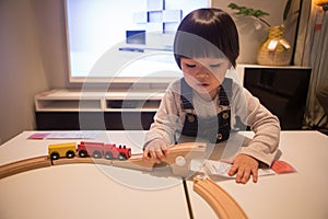 A boy in denim overalls is playing with a wooden train toy attentively