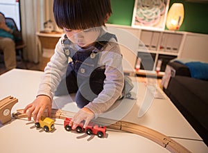 A boy in denim overalls is playing with a wooden train toy attentively