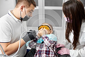 Boy in dental chair closes mouth with hands, fearing dentist