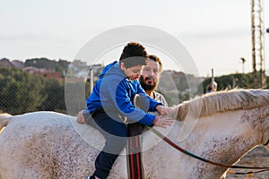 Boy with disabilities riding a horse during an equine therapy session with a male instructor.