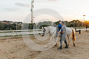 Boy with disabilities riding a horse during equine therapy session outdoors.