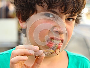 Boy with disgust grimace hold unusial strange thai food roasted insects
