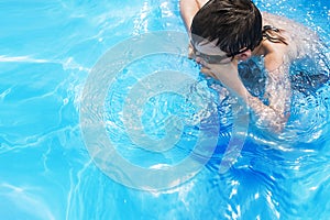 Boy dives in swimming pool with swimming glasses. boy swims in the pool.