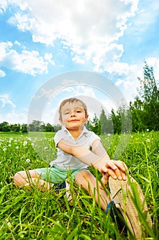 Boy does gymnastics while sitting on a meadow