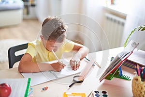 The boy does his homework at home. happy child at the table with school supplies concentrated writing in the retreat, doing