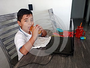 Boy does home school with his laptop and uniform in the dining room and eats a sandwich at break time and rest inside his house in