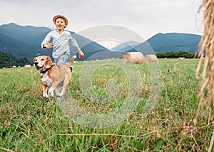 Boy and dog run together on the field with haystacks