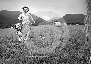 Boy and dog run together on the field with haystacks