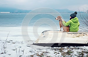 Boy with dog sitting together on the old boat near winter lake