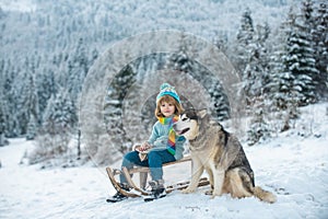 Boy with dog sledging outside in winter. Kids in snow.