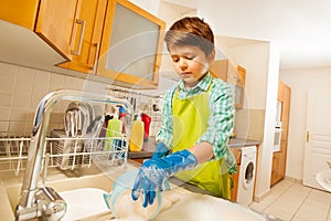 Boy doing the dishes under running water in sink