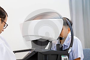 Boy doing eye test checking examination with autorefractor in optical shop, Optometrist doing sight testing for child patient, Eye