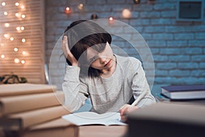 Boy is doing homework surrounded by books at night at home.