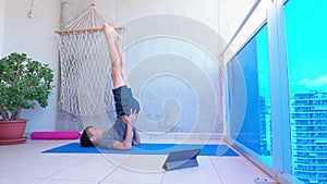 Boy doing sport exercises while watching video lesson online on tablet computer on balcony. Sport, healhty lifestyle