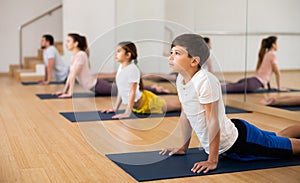 Boy doing stretching asana Bhujangasana during family yoga class