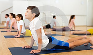 Boy doing stretching asana Bhujangasana during family yoga class