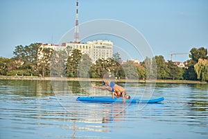 Boy doing yoga exercises while swimming on paddle board in lake.