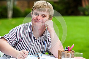 Boy with down syndrome at desk holding glasses.