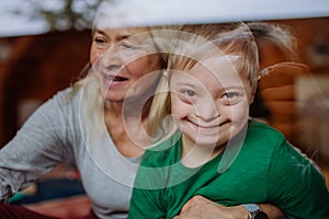 Boy with Down syndrome with his grandmother looking at camera through window at home.