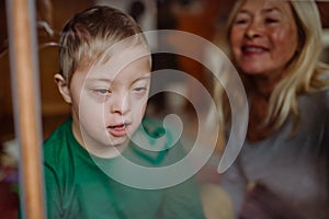 Boy with Down syndrome with his grandmother looking through window at home.