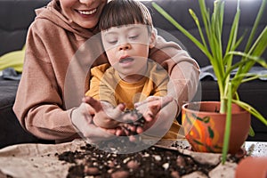 Boy with down syndrome holding ground at his hands while helping to his mother replacing flowers