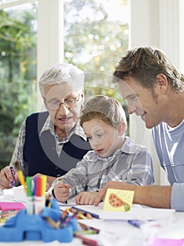 Boy Drawing With Crayons With Father And Grandfather