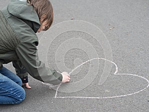 Boy draws heart with chalk on the ground